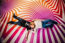 Couple lies on their backs atop a vibrant, trippy piece of art in Manhattan, NY, with their heads positioned in a yin yang shape, creating a creative and harmonious engagement portrait.