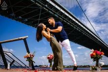He dips her gracefully at Race Street Pier in Philadelphia, their hands clasped as the expansive river and sky create a dramatic backdrop beneath the towering bridge for this romantic portrait.