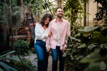 An engaged couple smiles while navigating pathways inside the tropical plant conservatory at Jardin Botanique de Metz in Moselle, France.