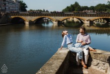 An engaged couple rests at the water edge while enjoying peaceful views along the river in Metz, France.