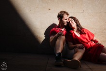 An engaged couple cuddles together on the grass while glowing afternoon sun filters through trees in Metz, France.