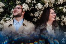 An engaged couple nestles under a canopy of vibrant pink spring blossoms in a park in Metz, Moselle, France.