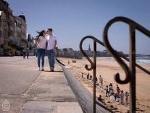 Engaged couple kisses while walking along the seaside promenade above the beach during their engagement weekend in Saint-Malo, Brittany, France.
