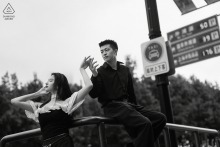 An engaged couple reaches toward each other while waiting beside a city transit shelter during an evening street session along The Bund in Shanghai, China.