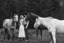 Engaged couple stands among the groom’s horses during a Western lifestyle engagement session in Sandpoint, Idaho.