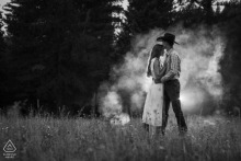 Engaged couple embraces in a field surrounded by drifting smoke during a Western lifestyle engagement session inspired by wildfire-smoky skies in Sandpoint, Idaho.