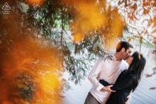 Engaged couple kisses beneath tree branches framed by warm orange foliage during a portrait session in San Francisco, California.