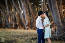 In San Francisco, a couple poses for an engagement portrait with a row of trees behind them.