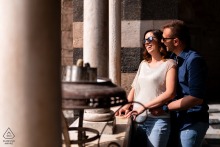 On the Amalfi Coast in Italy, a couple shares a hug in the sunlight, the bright afternoon light illuminating their figures and creating sharp contrasts with the surroundings.