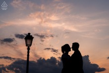 In Trieste, Italy, a silhouette of a couple stands against the vibrant sky, their forms outlined by the golden light of sunset, creating a dramatic and intimate portrait of their bond.