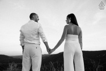 An engaged couple stands hand in hand overlooking the scenic landscape during a black and white engagement session in the Gorges de l'Ardèche, France.