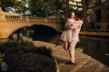 Pre-wedding engagement portrait of a couple sharing a joyful embrace beside the San Antonio River Walk in the warm glow of evening light.