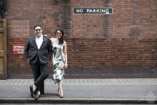 Pre-wedding engagement portrait of a stylish couple walking together along a London, England, street with an urban backdrop.