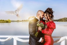 Pre-wedding engagement portrait of a couple embracing beside the water in Bucharest, Romania, with a white dove soaring above them.