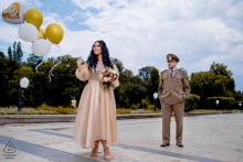 Pre-wedding engagement portrait of a couple in Bucharest, Romania, with the bride holding white and gold balloons as the groom stands nearby.
