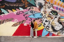 An engaged couple embraces in front of a striking street art mural during their engagement portrait session in Union Square, Somerville, Massachusetts.