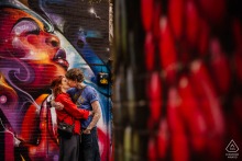 Pre-wedding engagement portrait of a couple kissing beside bold urban street art in Manchester City Centre, England.