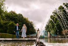 A couple walks along the pond at Rhinefield House in Hampshire, England, during an engagement portrait session at the venue chosen for their wedding.