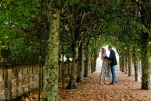 An engaged couple embraces beneath a tree-lined walkway during a pre-wedding portrait session at Rhinefield House in Hampshire, England.