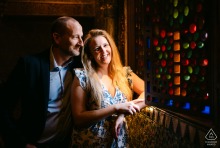 Soft window light illuminates an engaged couple beside a stained glass window at Rhinefield House in Hampshire, England, during their pre-wedding portrait session.