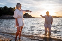 A couple playfully splashes and points at each other in the water during a golden hour engagement portrait at La Madrague, Var, France.