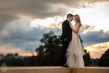 Golden sunset light surrounds a couple embracing beneath stormy skies during their engagement portrait session at the Philadelphia Museum of Art in Philadelphia.