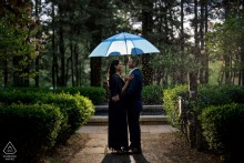 Pre-wedding engagement portrait of a couple beneath a blue umbrella at Ridley Creek State Park in Newtown Square, Pennsylvania, with shimmering rain creating a cinematic atmosphere.