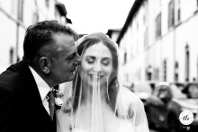 In Chiesa Santa Reparata, Terra del Sole, Italy, the father of the bride gives his daughter a tender kiss just before they enter the ceremony, sharing a touching moment of closeness and support.