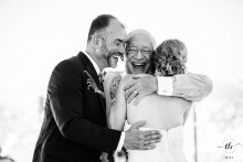 During a backyard wedding in Grosse Ile, Michigan, the bride and groom share a joyous embrace filled with laughter with the bride's father after his heartfelt afternoon toast.
