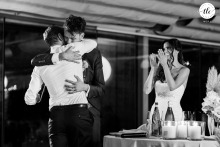 In Jesolo, Veneto, Italy, the groom hugs his friend after a heartfelt speech while the bride applauds nearby, reflecting joy and gratitude during the wedding celebration.