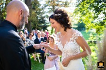 In the picturesque grounds of Villa Bodo Sommariva in Moncrivello, Vercelli, the bride smiles as she slips the ring onto the groom's finger during a tender outdoor wedding moment.