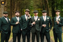 A striking wedding photo of groom and groomsmen in deep forest green suits posing with cigars at Poplar Springs Manor in Warrenton, VA, surrounded by lush trees creating a sophisticated and timeless image.