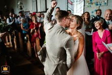 At Southwood Hall, Norwich, Norfolk, UK, the groom joyfully punches the air while sharing his first kiss with his wife.