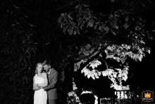 At Elms Barn, Norfolk, a bride and groom embrace in a nighttime portrait. The black-and-white shot features an illuminated tree in the background.
