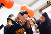 Groom at home in Shanghai, China, is playfully hit by orange props during lively wedding games, guests laughing joyfully.