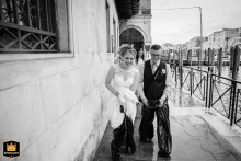 At Palazzo Cavalli, Venice, Italy, a laughing couple exits the Mayor's House after their ceremony, navigating high water with garbage bags on their legs.
