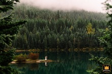 On a moody morning at Snoqualmie Pass, WA, a bride and groom stand distantly on a small peninsula within a lake.