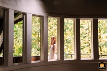At a cabin in Deming, WA, a bride stands on the balcony, looking inward through a series of repeating vertical windows.