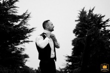 Black and white WPJA photo: A groom prepares on a misty Mt. Baker, WA mountaintop, dramatically framed by trees.