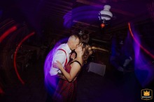 A couple kisses on the Budapest reception dance floor, surrounded by swirling purple and red lights, radiating festive party energy.