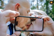 A joyful couple kisses at Hotel Park, Budapest, their faces creatively magnified and framed through a smartphone in playful wedding style.