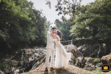 The bride and groom embrace in front of a pretty waterfall in Salies-de-Béarn, France. This intimate scene is captured next to the family home, a romantic setting for their union.