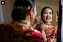 A smiling bride at No. 5 Hamilton Place uses a large ornate mirror to put on an earring. The reflection captures the excitement and joy of her final preparations before the wedding.