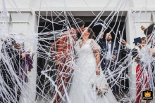 Exiting Ceremony, a Shower of Confetti for the Newlywed Couple A documentary-style photograph captures a joyful moment as a newlywed couple exits their religious ceremony in the Basque Country, France. The image shows the bride and groom surrounded by an explosion of confetti and white ribbons.