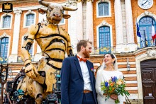 At the Place du Capitole in Toulouse, a wedding photographer captures a unique moment. The newlyweds stand before a giant Minotaur statue, a powerful and singular portrait of their day.