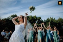 Hungary is the backdrop for a joyful bride throwing her bouquet mid-air under a bright blue sky, capturing the excitement and laughter of the tradition for her waiting guests.