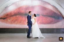 Bride and groom in the Parisian subway, standing in front of a wall with giant lips artwork, creating a graphic and artistic portrait.