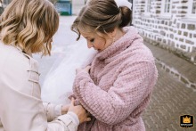 In Hülscheid, Schalksmühle, Sauerland, Germany, the bride wraps herself in a bathrobe after a couple’s outdoor photo session, her expression hinting at relief from the chilly air and adding a cozy touch to the day.
