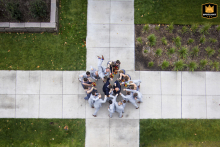 At the Walker Museum of Art in Minneapolis, MN, a drone captures the entire wedding party converging around the couple at a sidewalk intersection, creating a dynamic and celebratory aerial scene of urban togetherness.