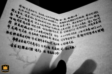 A black-and-white detail shot from Kaifeng, Henan, captures delicately held vow cards in the hands of the couple, focusing on the elegant script and the emotional significance of the promises exchanged.